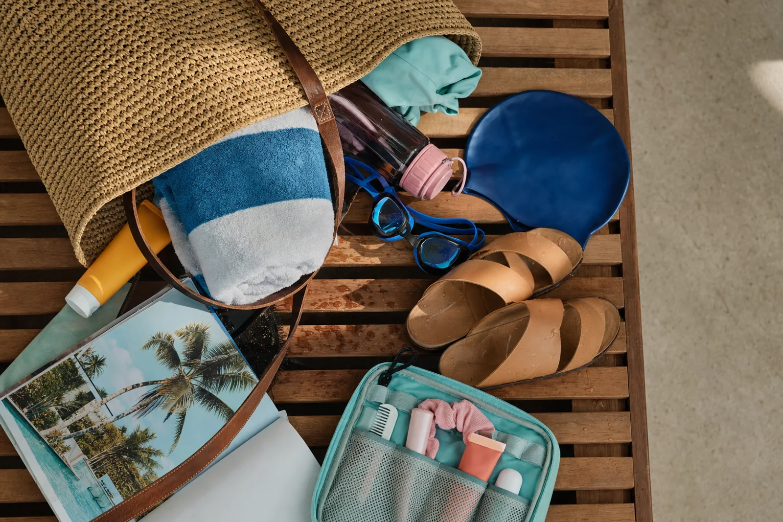 Volledige zwembad-tas inhoud uitgespreid met handdoek, goggles en sunscreen
